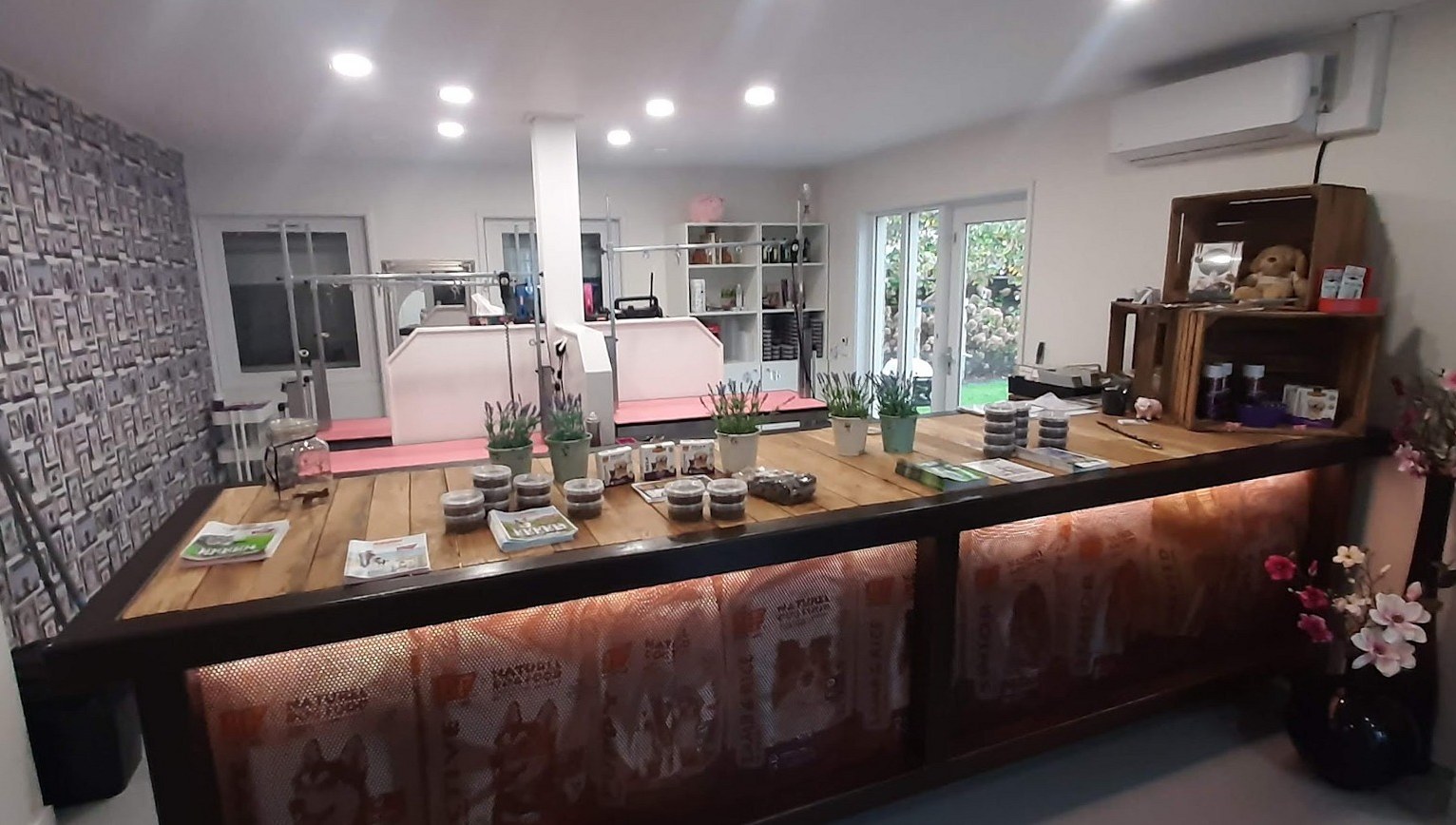 De salon: een lange houten toonbank met hondenvoer, daarachter de roze trimtafels en badkuipen